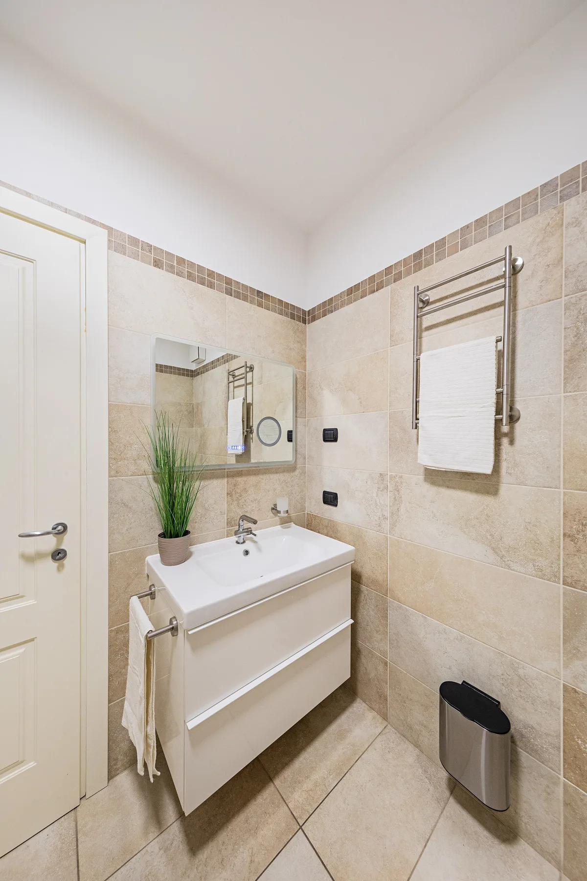 Un baño con azulejos, lavabo con mueble, espejo y toallero calefactable.