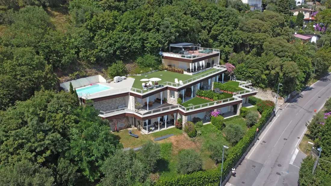 Un edificio moderno de varios niveles se encuentra entre árboles junto a una carretera pavimentada.