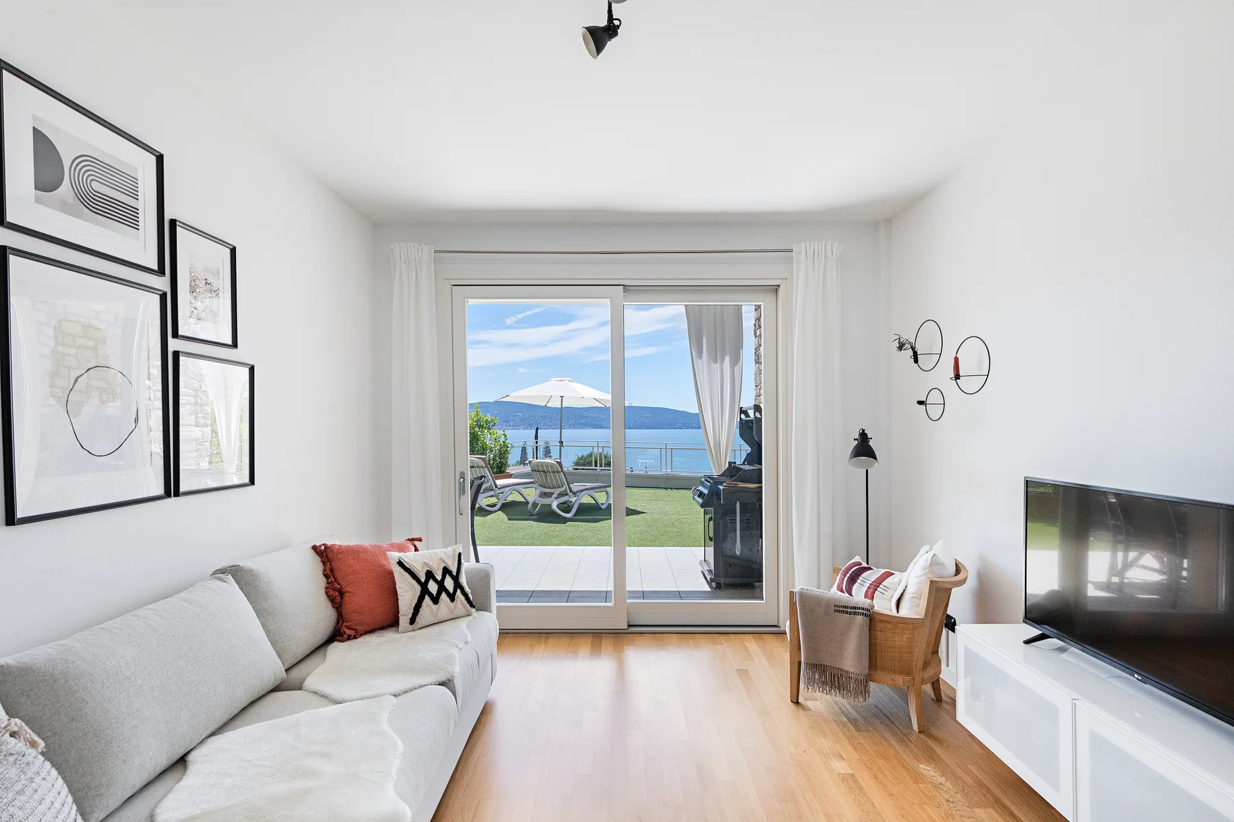 Una sala luminosa con sofá, televisor y puertas corredizas de vidrio con vista al agua.