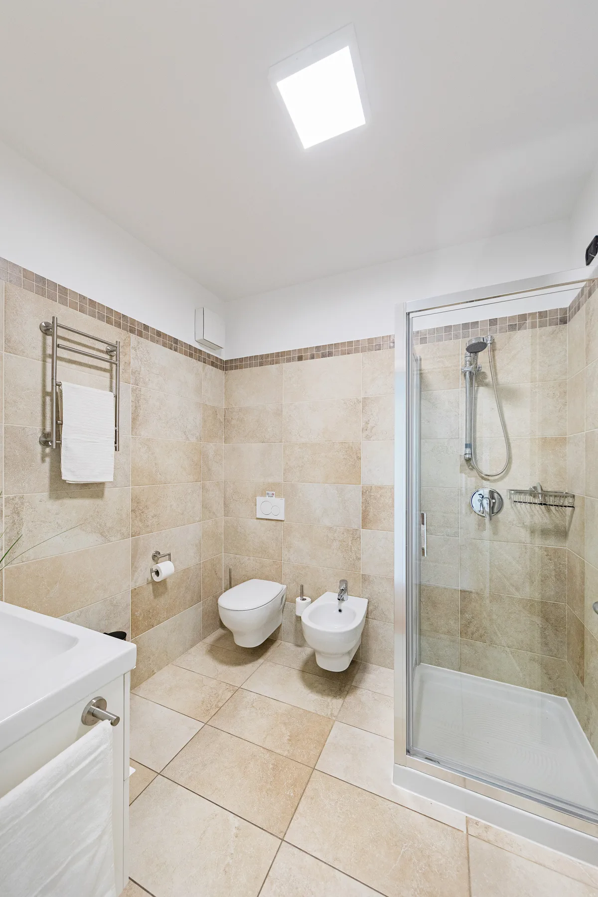 Un baño con azulejos, lavabo, inodoro, bidé y ducha de vidrio.