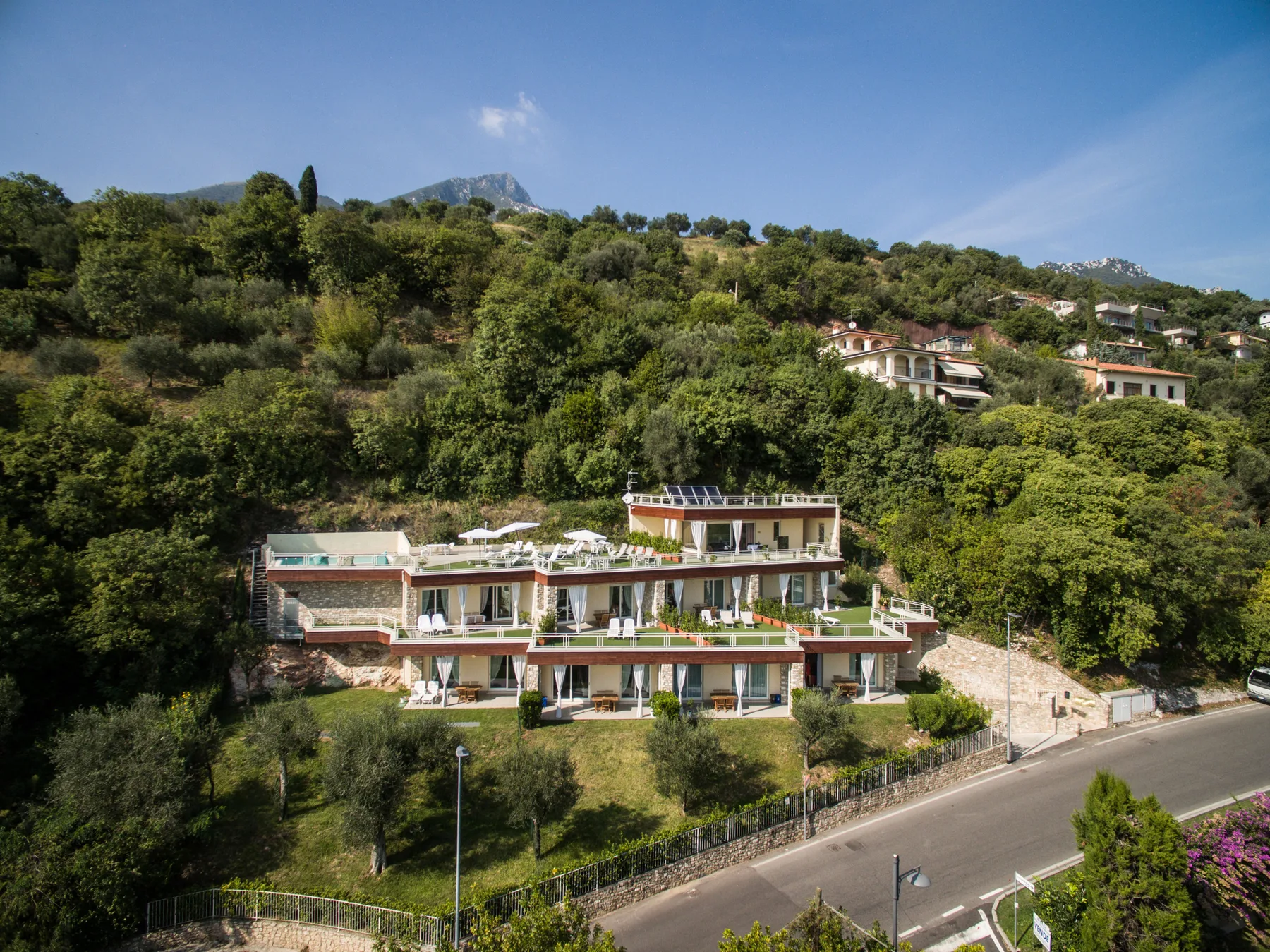 Un edificio de varios niveles está junto a una carretera, al pie de una ladera verde.