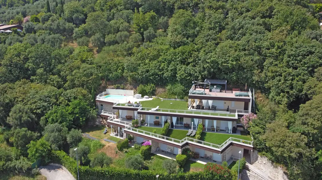 Un edificio moderno con terrazas ajardinadas se encuentra entre densos árboles verdes.