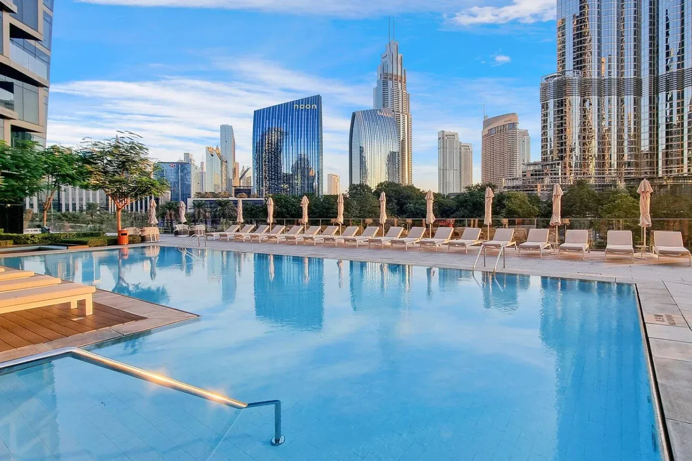 A rooftop swimming pool overlooks a city skyline, with lounge seating along the deck.