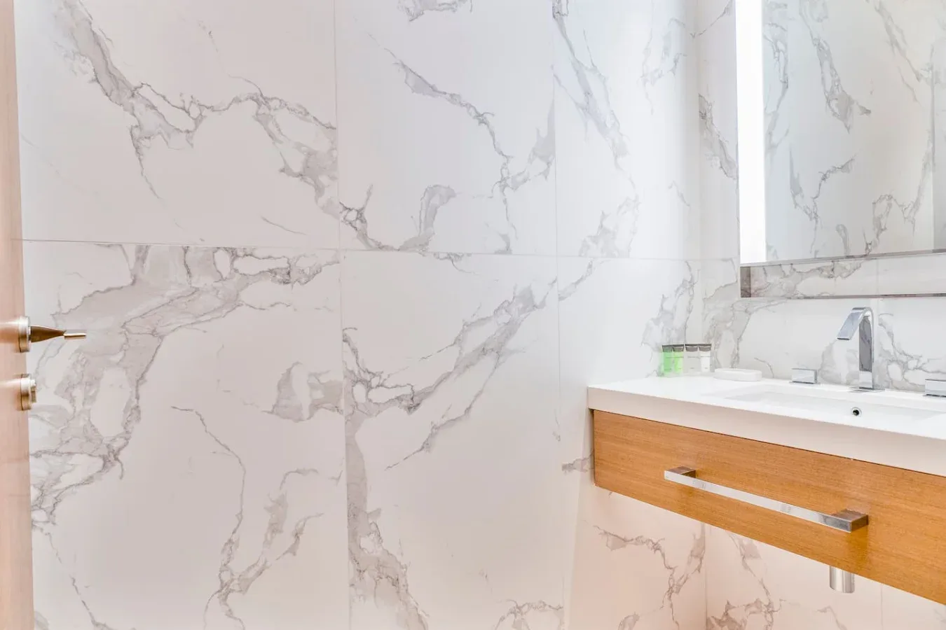 A bathroom vanity with a faucet sits beside large white marble-patterned wall panels.