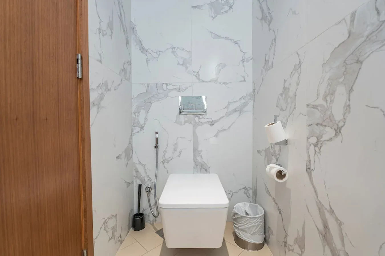A bathroom with a toilet and marble-patterned wall panels.