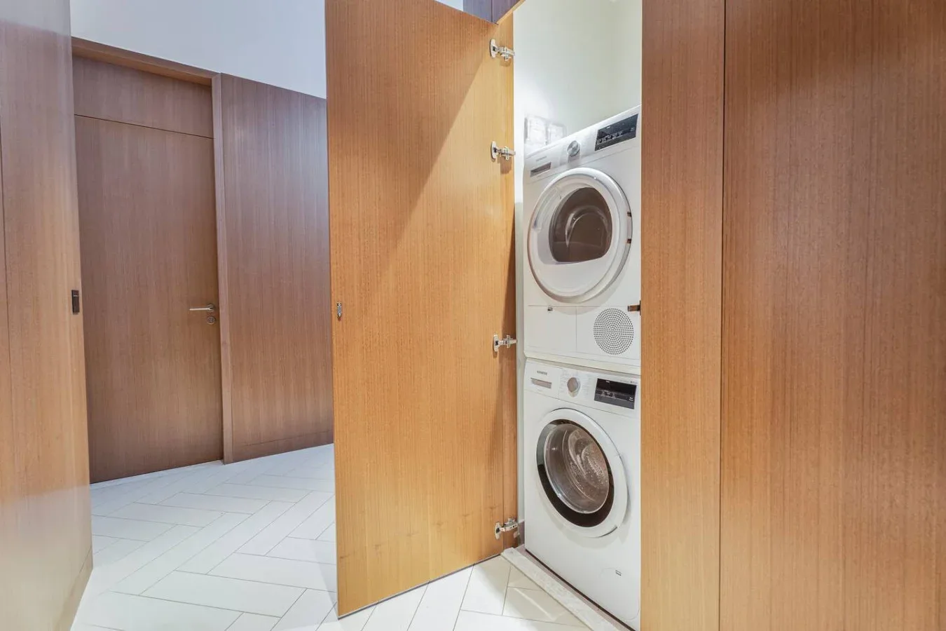 A laundry area with a stacked washer and dryer behind an open wooden door.