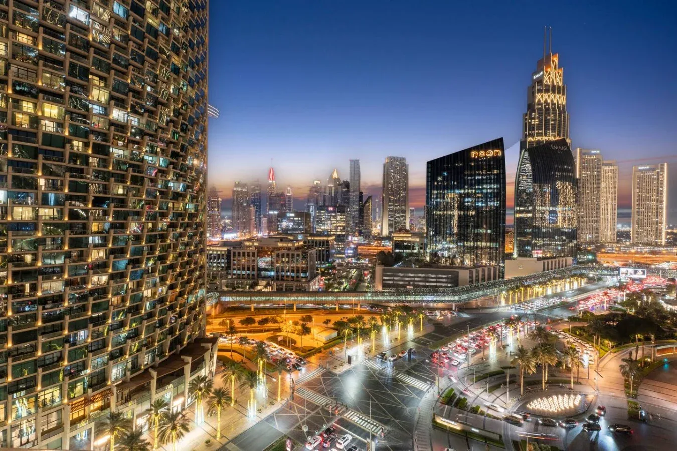 A city skyline at dusk overlooks illuminated buildings and busy roads.