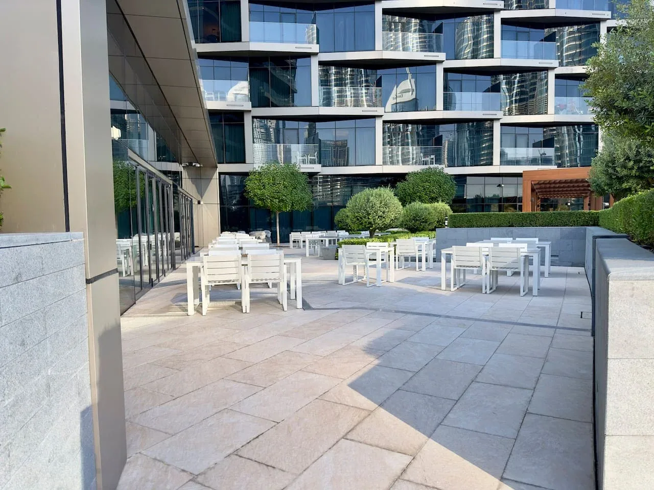 An outdoor terrace with white tables and seating beside a modern glass building.