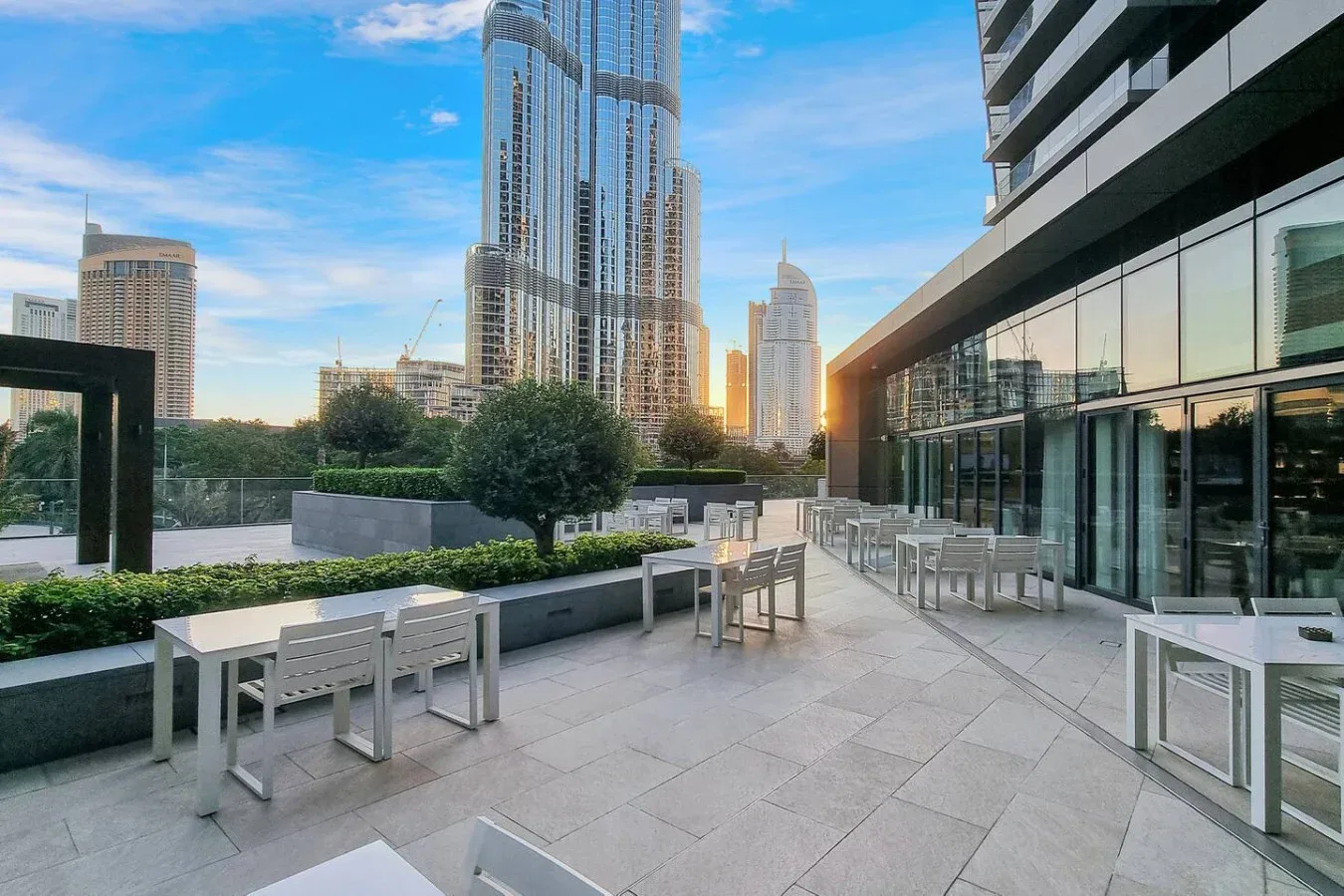 An outdoor terrace with tables and seating beside a glass-fronted building.