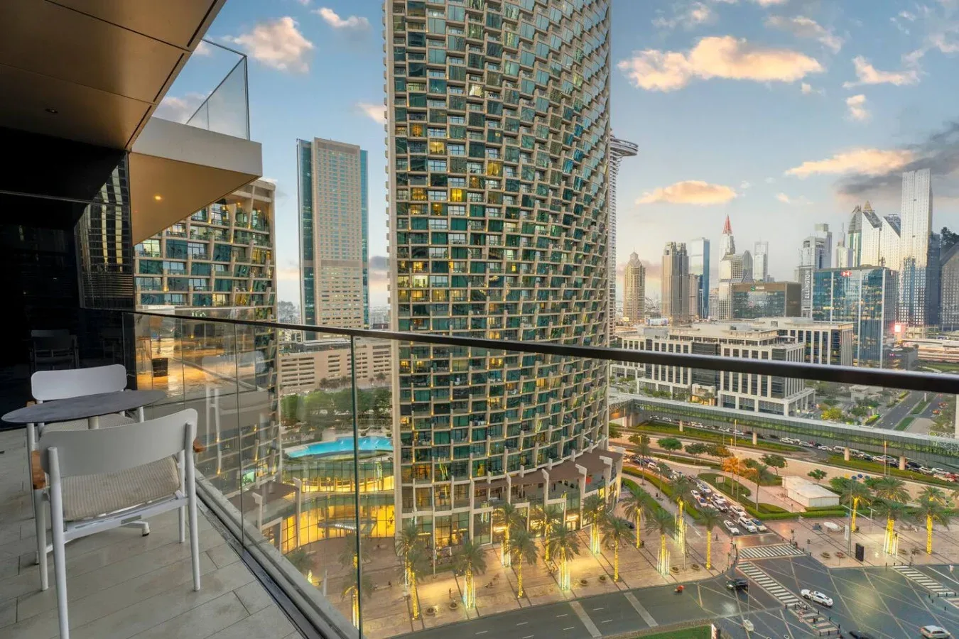 A high-rise balcony overlooks modern towers, streets, and landscaped grounds.