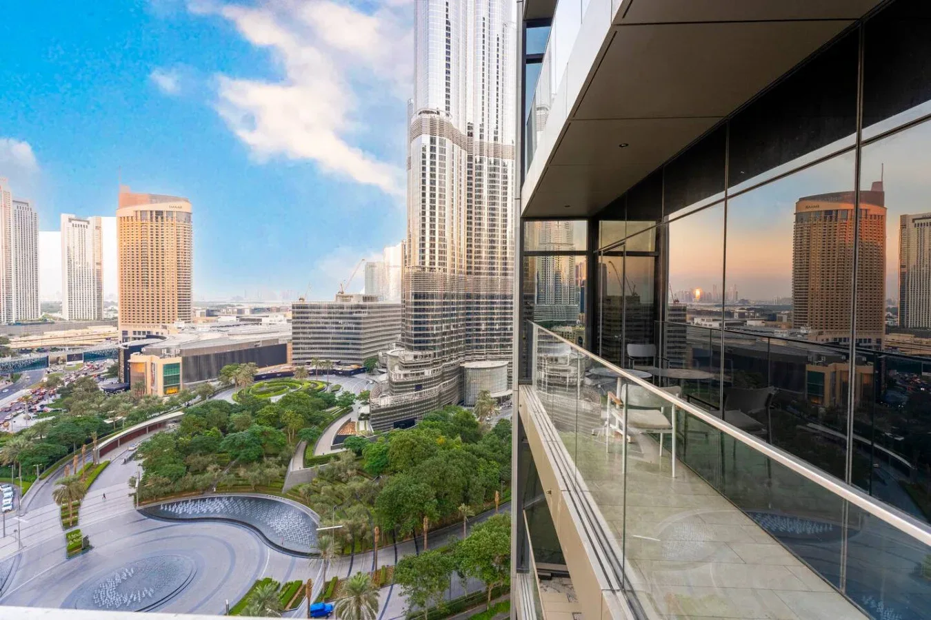 A city skyline and landscaped park are seen from a glass-fronted balcony.