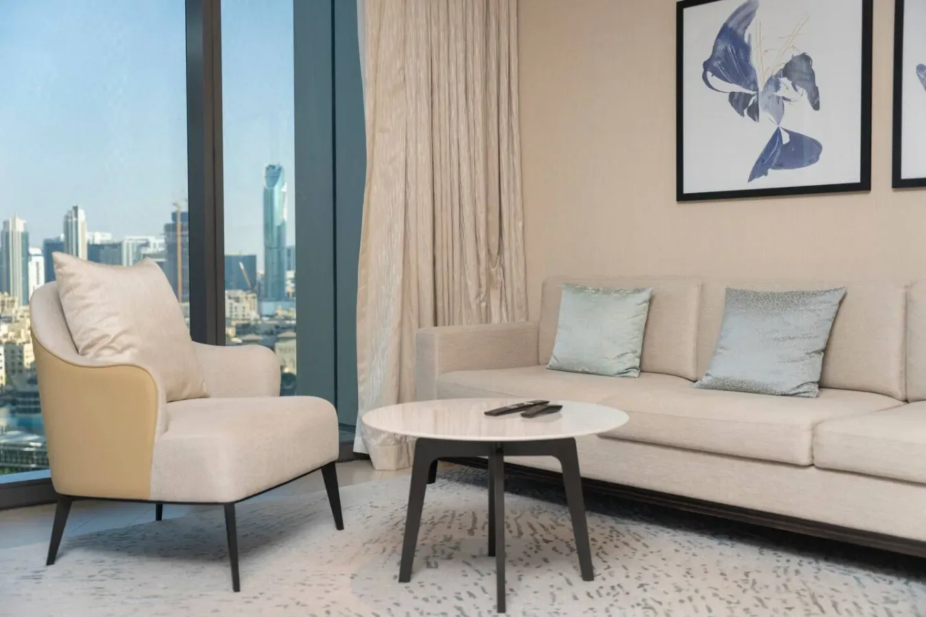 A bright living room with pale seating beside large windows overlooking the city.