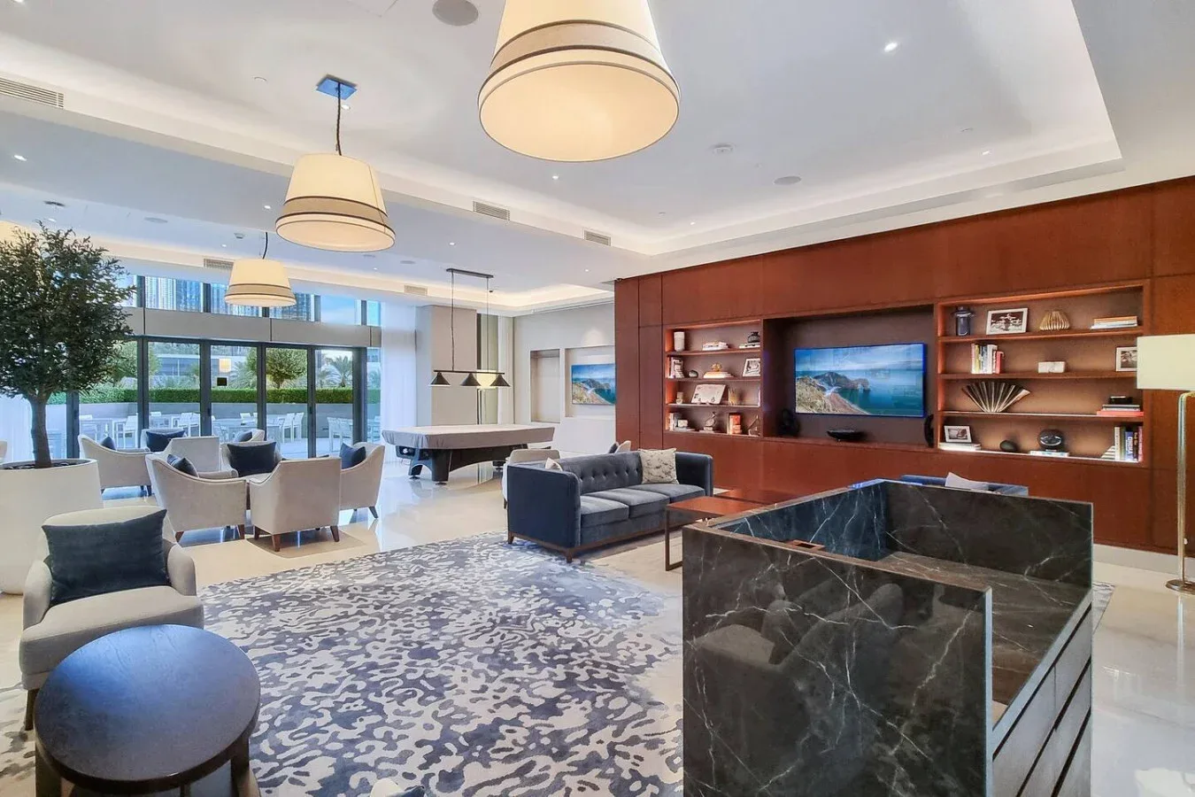 A spacious lounge with seating, a patterned rug, and a large built-in shelving wall.