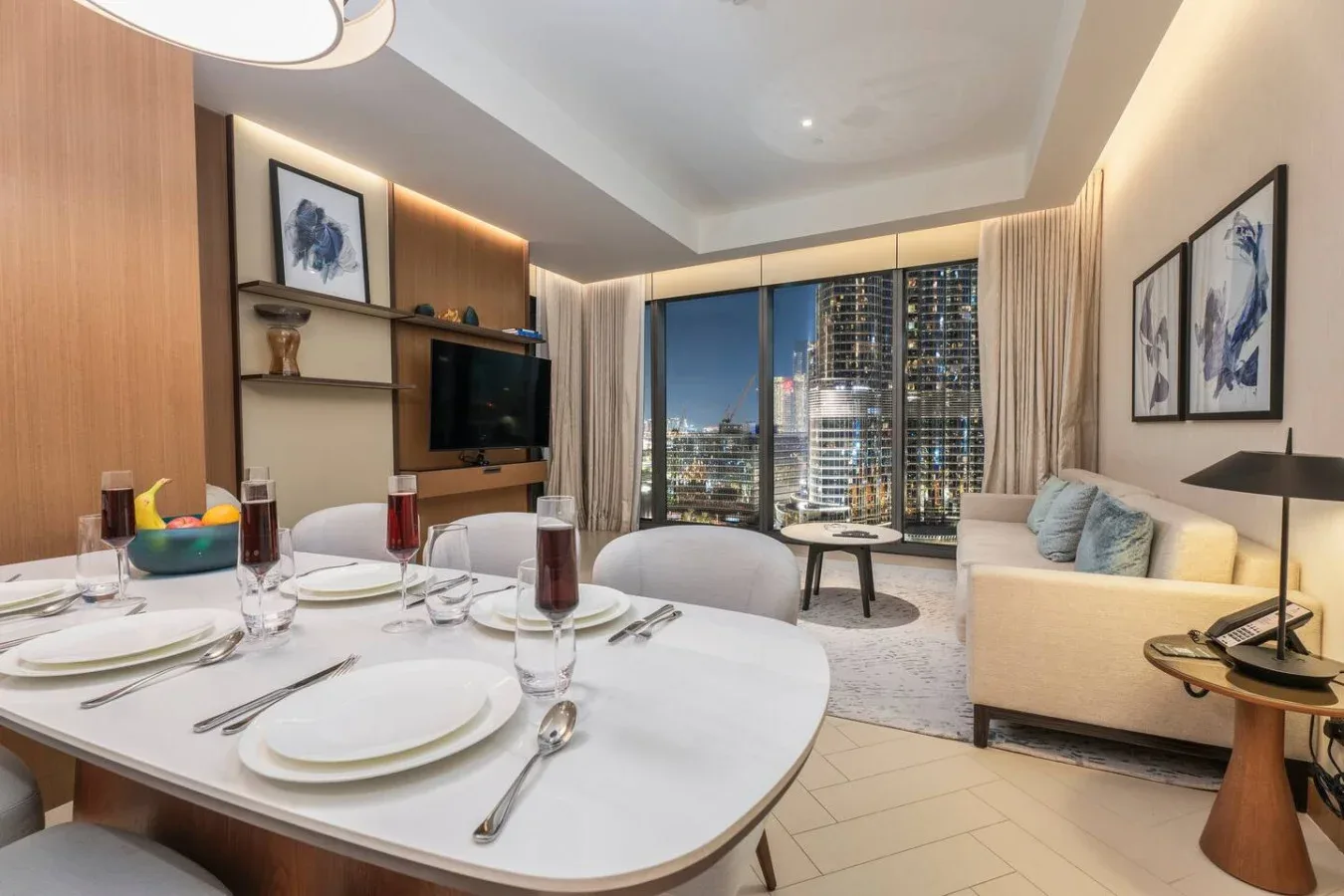 A dining area and lounge with a set table and large windows overlooking city buildings.