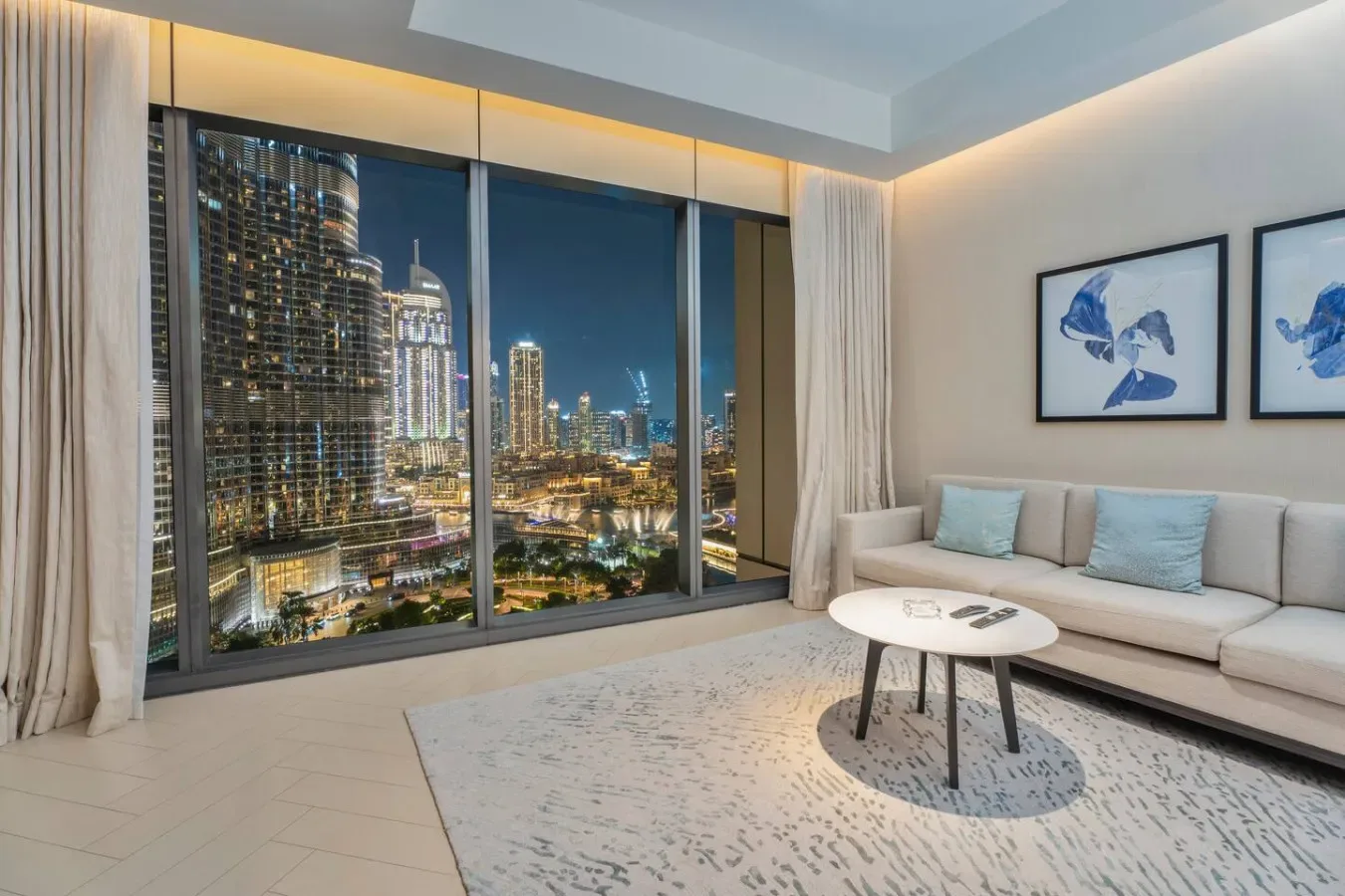 A living room with a light-colored seating area and city views through large windows.