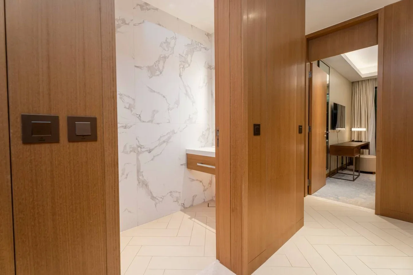 A wood-paneled hallway opens to a marble-accented bathroom and a furnished room.