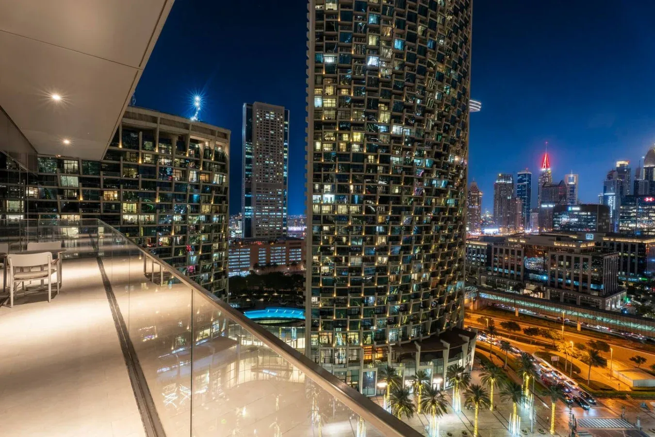 A nighttime city skyline viewed from a lit balcony.