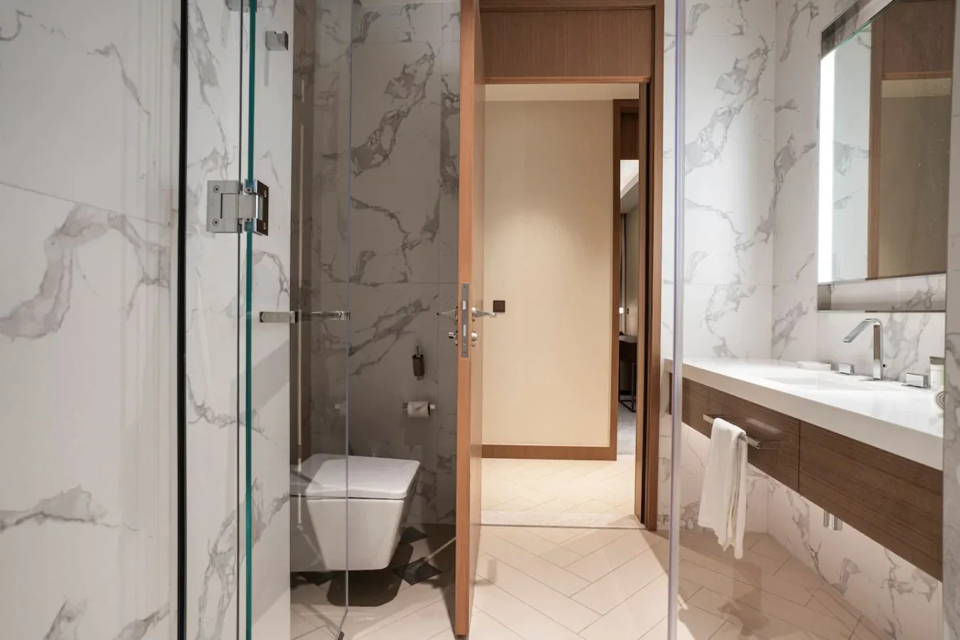 A bathroom with a glass shower, toilet, and vanity beside an open doorway.
