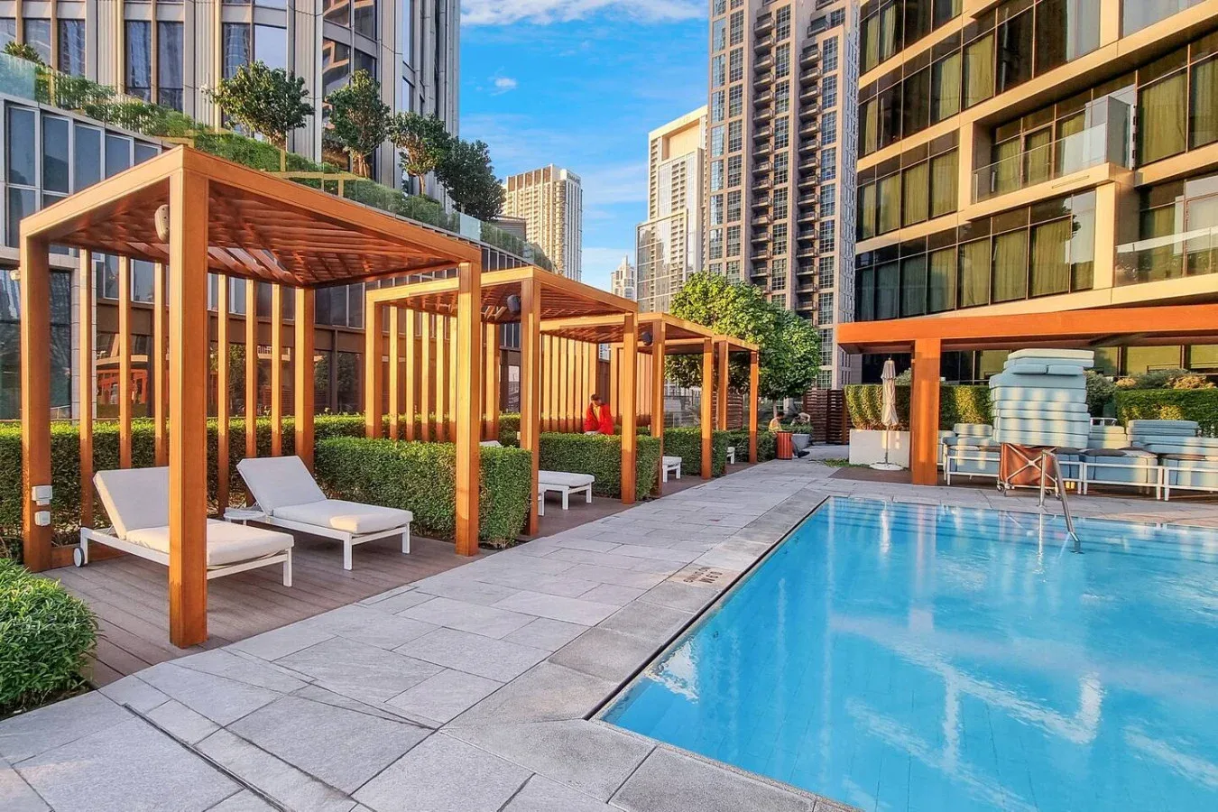 An outdoor swimming pool beside wooden pergolas and seating in a high-rise courtyard.