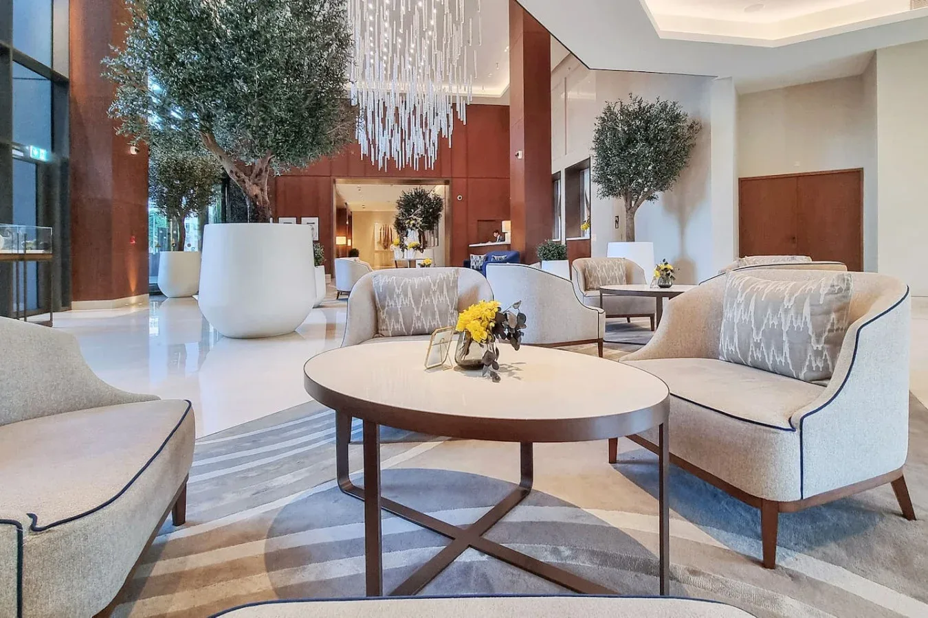 A spacious hotel lobby with lounge seating, tables, and indoor trees.