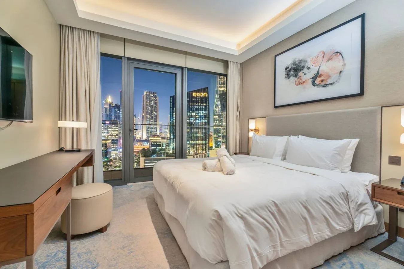 A bedroom with a neatly made bed and city views through large windows.