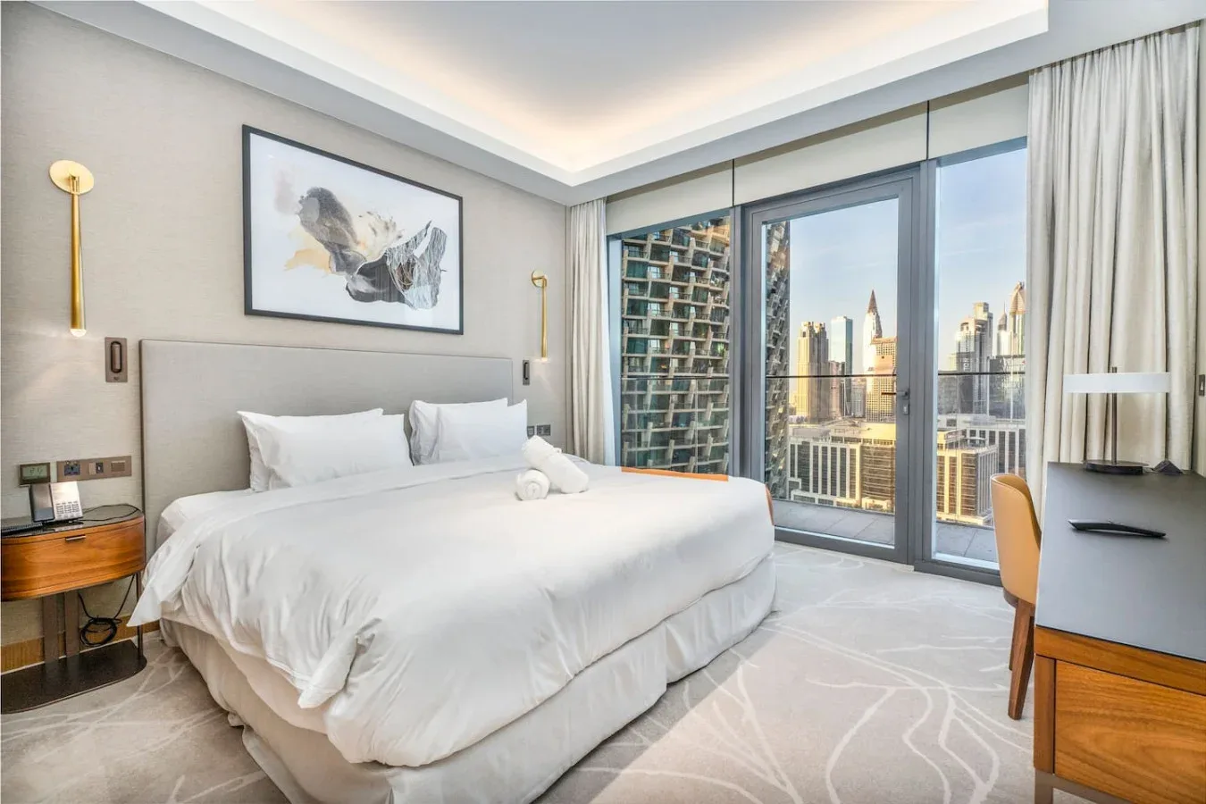 A bedroom with a neatly made bed beside large windows overlooking the city.