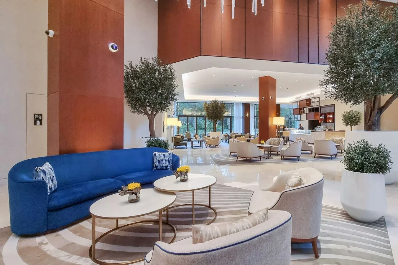 A spacious hotel lobby with lounge seating and large potted trees.