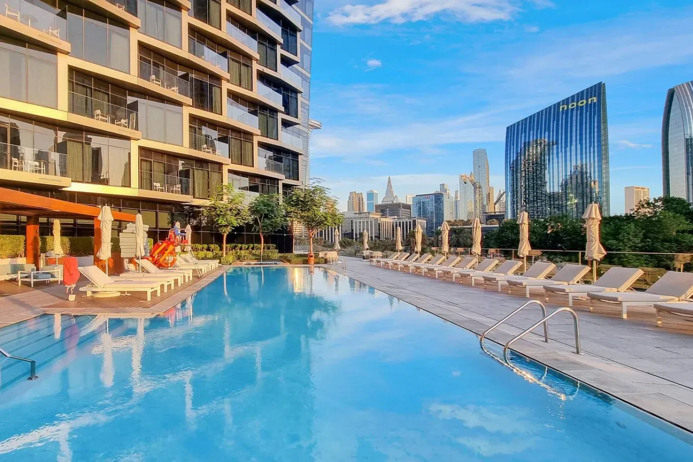 A rooftop swimming pool overlooks nearby high-rise buildings and the city skyline.