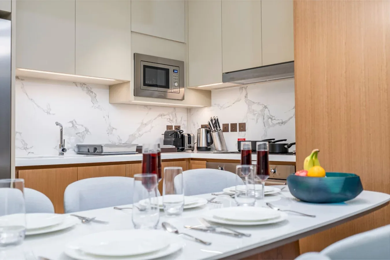 A modern kitchen with pale cabinetry, a marble-patterned backsplash, and a dining table.