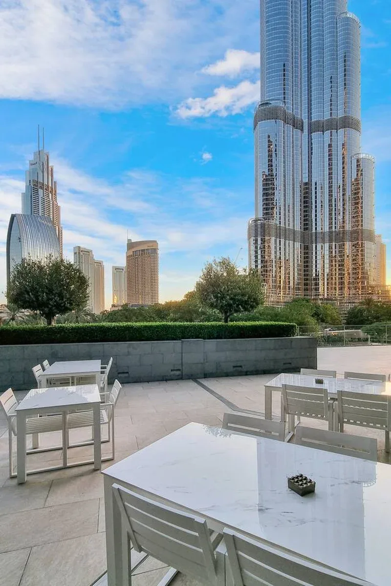 An outdoor dining terrace overlooks landscaped greenery and a city skyline.