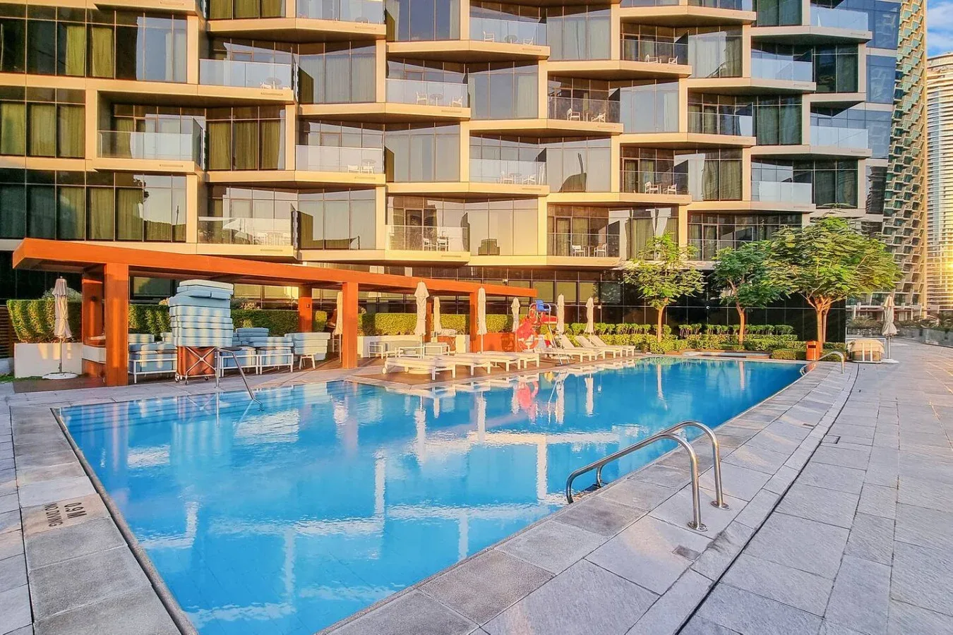 An outdoor swimming pool sits beside a modern building and paved deck.