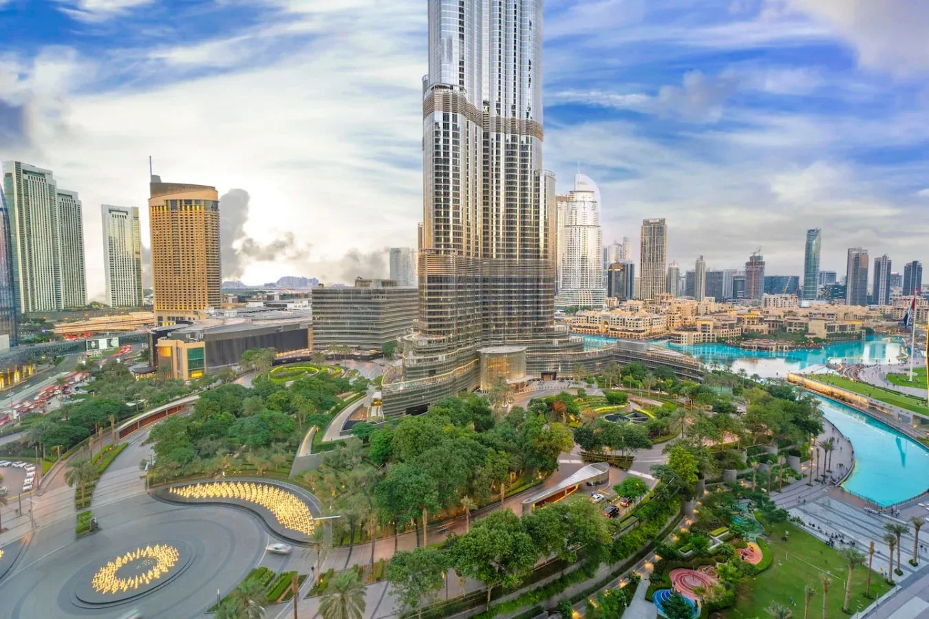 City skyline with a very tall central tower overlooking landscaped grounds and a curved pool.