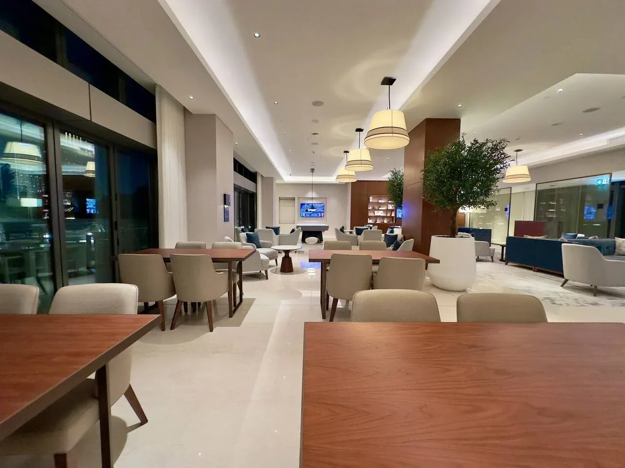 A spacious lounge with seating, tables, and a large indoor tree.