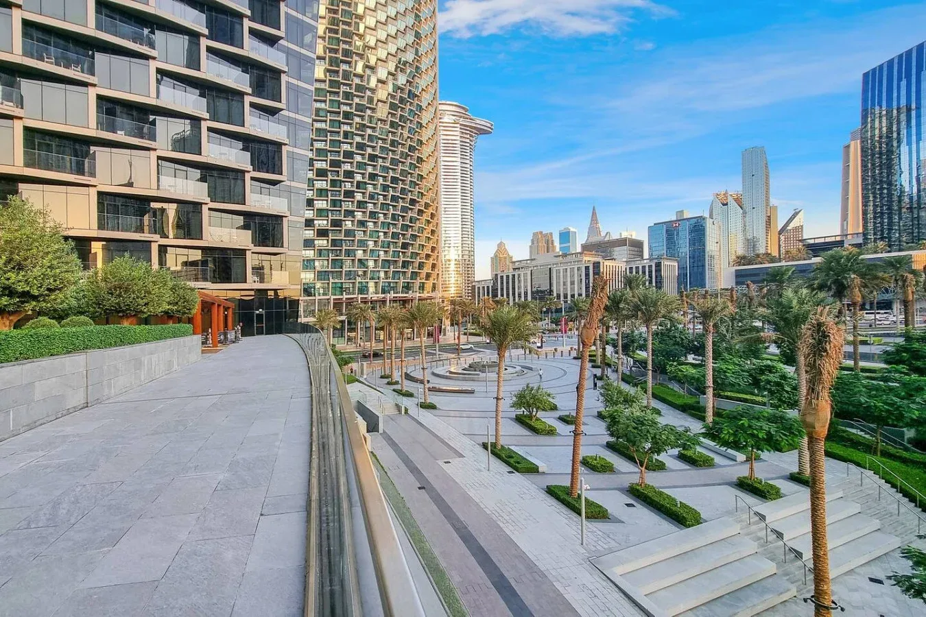 A landscaped urban plaza with paved walkways, greenery, and high-rise buildings.