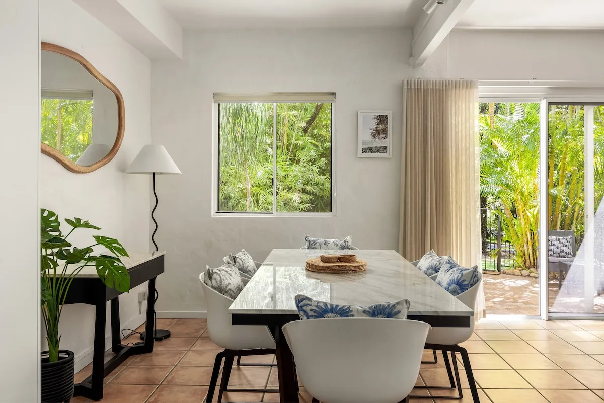 A bright dining area with a table, seating, and sliding glass doors opening to greenery.