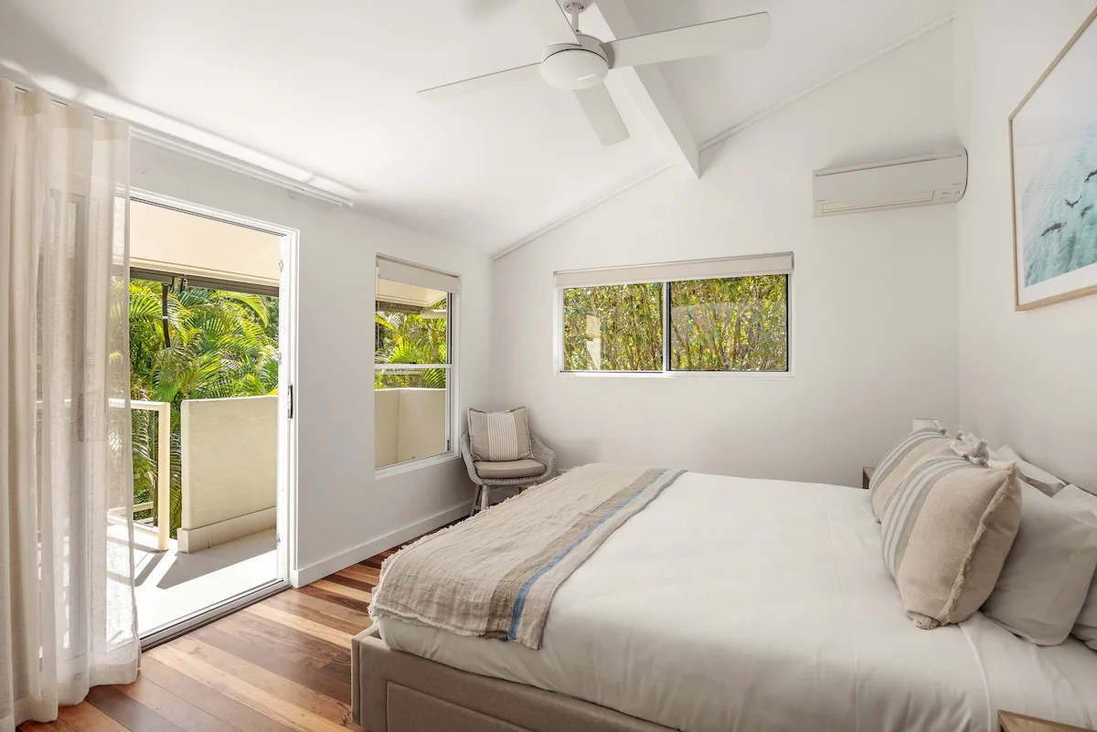 A bright bedroom with a large bed and windows overlooking greenery.