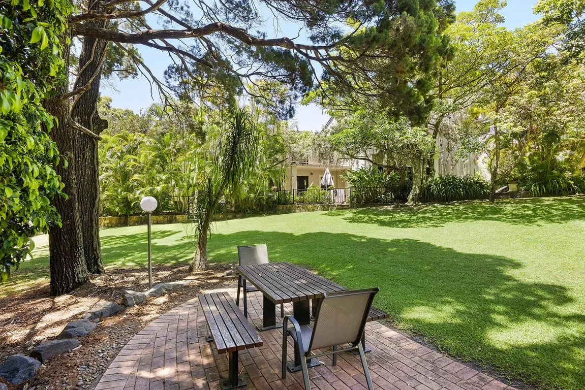 A leafy garden with a brick patio and outdoor seating.
