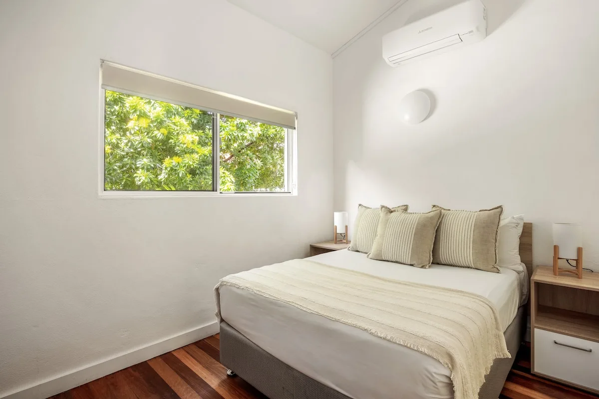 A bright bedroom with a bed, window, and air conditioner.