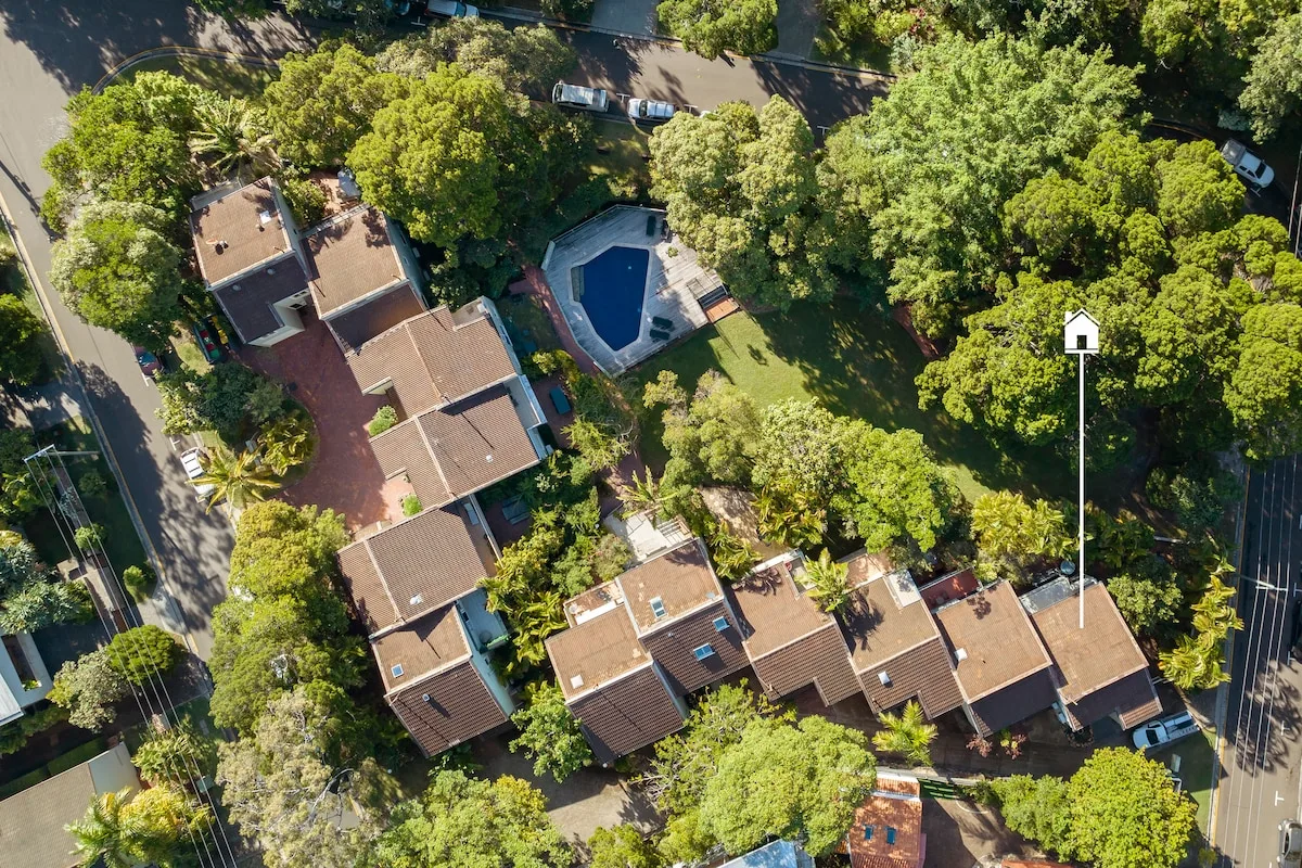 Aerial view of a cluster of buildings surrounded by trees, with a pool nearby.