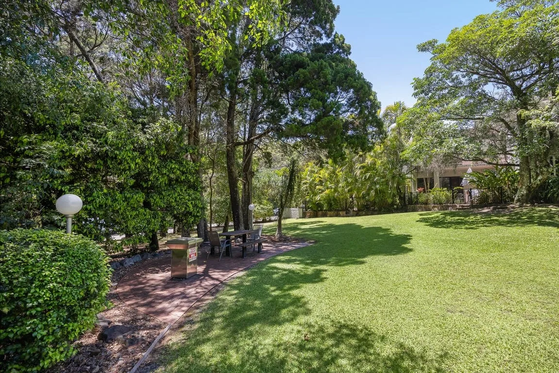 A landscaped garden with a lawn, mature trees, and a paved seating area.