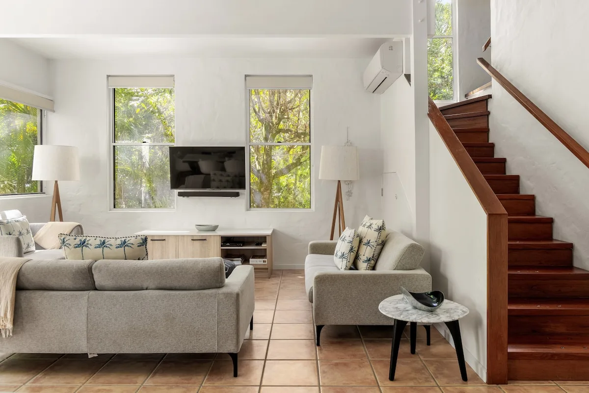 A bright living room with seating, a wall-mounted television, and stairs.