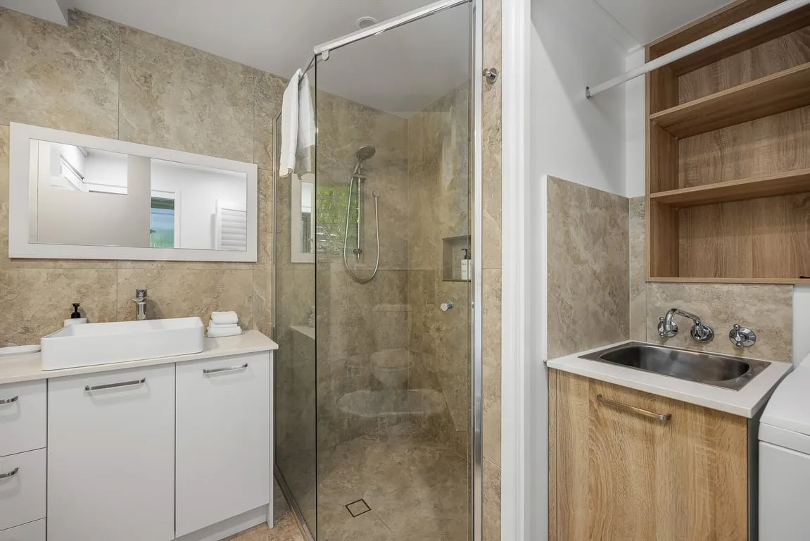 A bathroom with a glass shower, white vanity, and wood cabinetry.