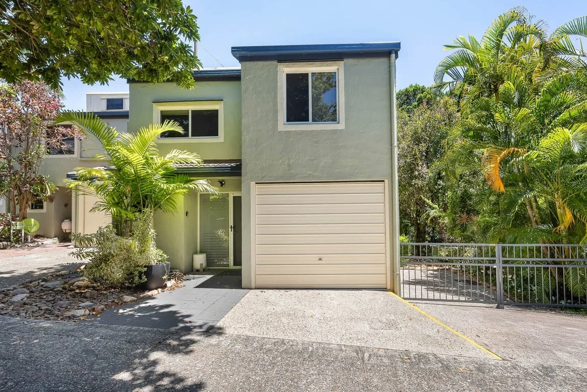 A modern house exterior with a garage and tropical landscaping.