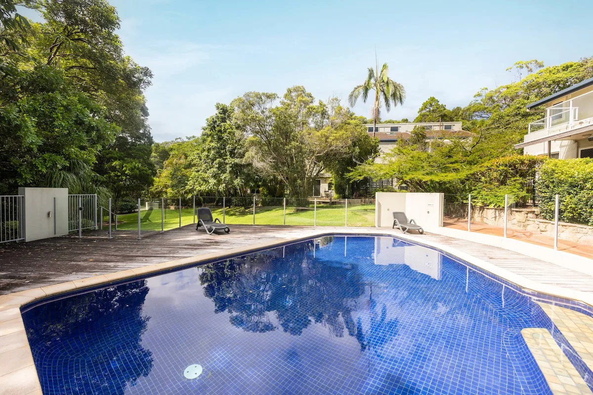An outdoor swimming pool beside a paved deck and green garden.