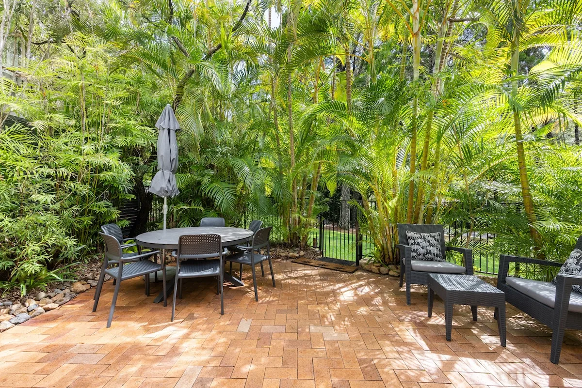 A brick-paved patio with outdoor seating and lush tropical greenery.