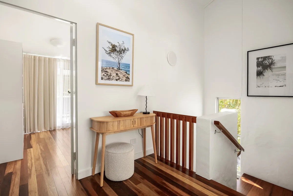 A bright hallway with a wooden console table and framed coastal artwork.