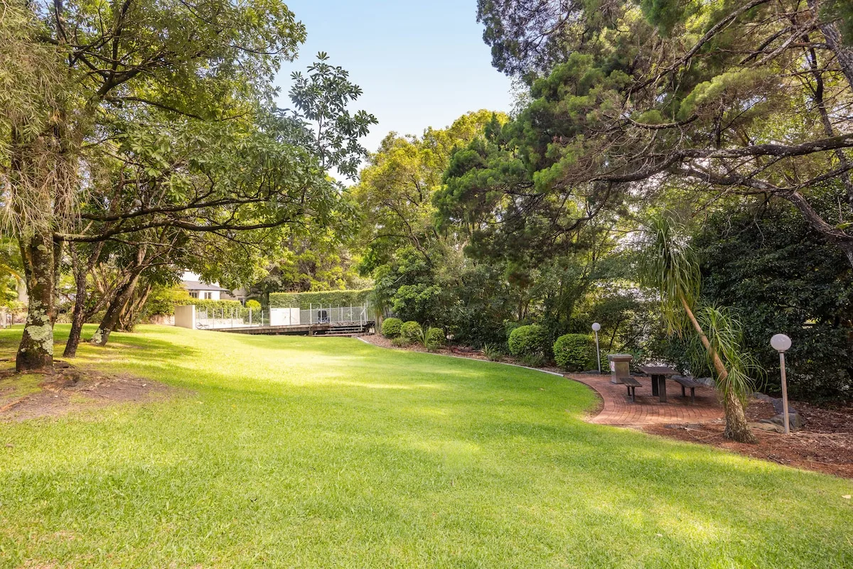A landscaped garden with a broad lawn, mature trees, and a small seating area.
