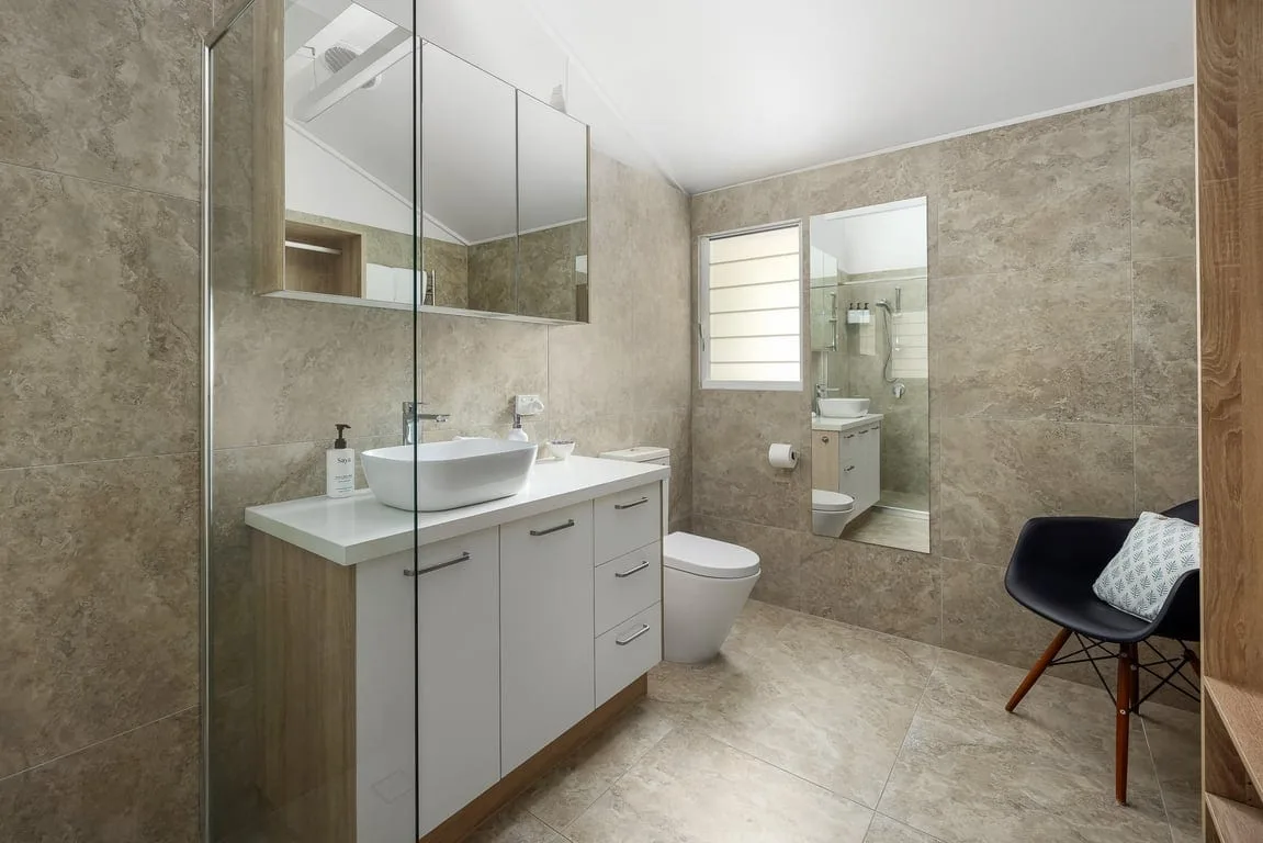 A tiled bathroom with a vanity, mirror, toilet, and seating.