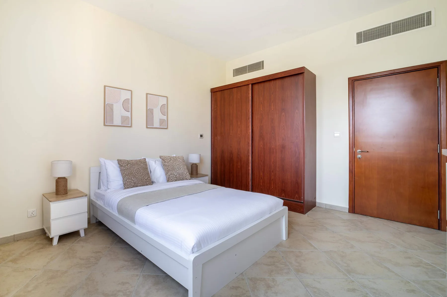 A bedroom with a neatly made bed and a large wooden wardrobe.