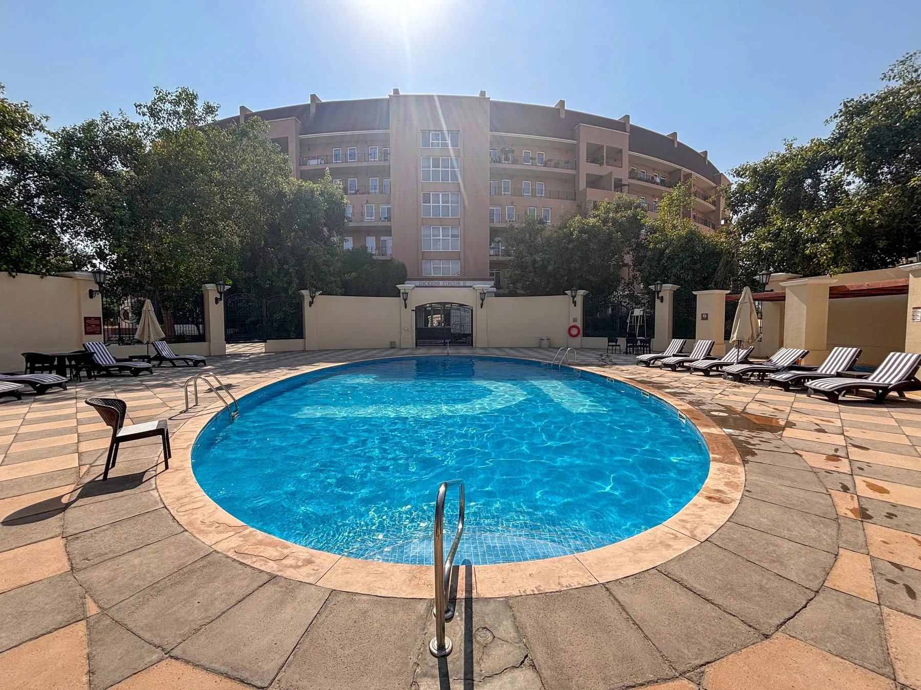 An outdoor swimming pool with lounge chairs on the surrounding paved deck.